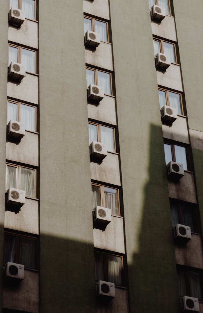 Vertical shot of a residential building featuring multiple air conditioning units in an urban setting.