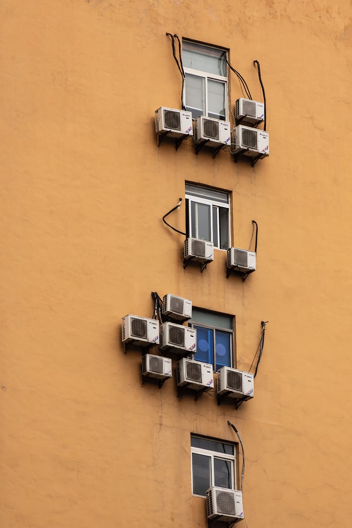 Yellow building facade with windows and numerous air conditioning units attached.
